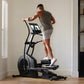Man wearing gray tank top and white shorts using black NordicTrack elliptical machine with digital display in home gym settin