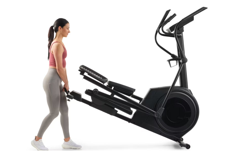 Woman in pink tank top and gray leggings using black NordicTrack AirGlide 7i elliptical with dual handles and large wheel on 