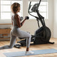 Woman performing lunge exercise with dumbbells on blue mat in front of black NordicTrack elliptical machine in home gym
