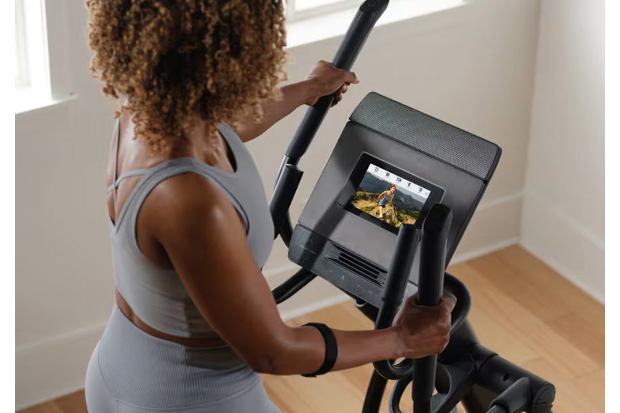 Person wearing gray sports bra using black NordicTrack AirGlide 7i elliptical with digital display screen