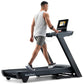 Man wearing white sleeveless tank and gray shorts running on NordicTrack black treadmill with digital screen display