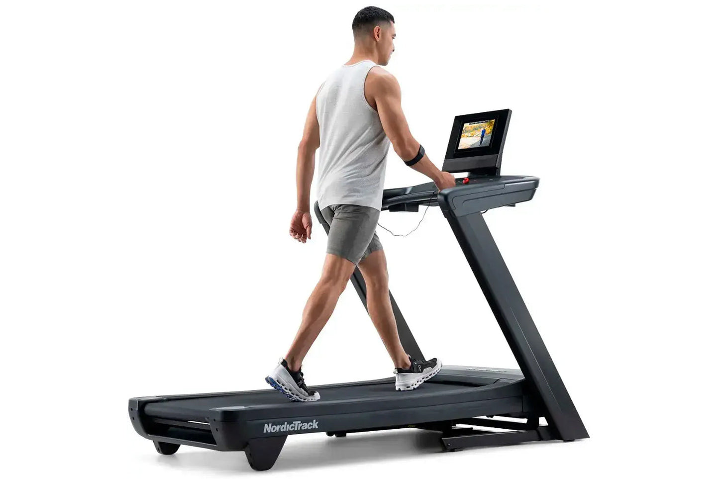 Man wearing white sleeveless tank and gray shorts running on NordicTrack black treadmill with digital screen display