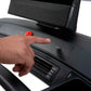 Hand pressing red emergency stop button on black treadmill console with incline controls