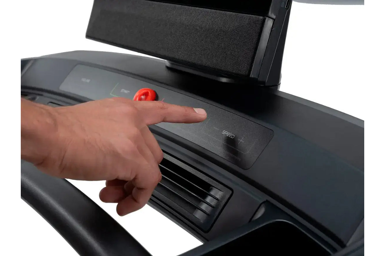 Hand pressing red emergency stop button on black treadmill console with incline controls