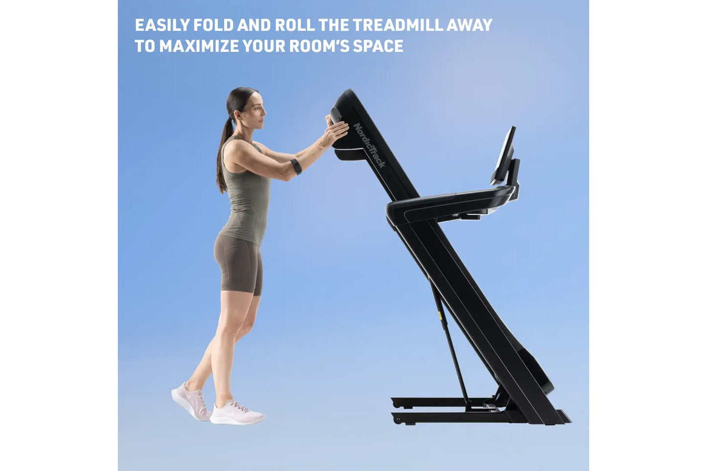 Woman in beige athletic wear folding black treadmill with digital display against blue background