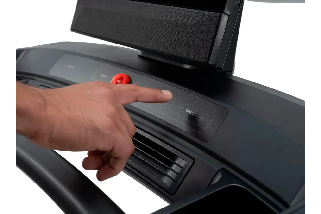 Hand pressing red emergency stop button on NordicTrack treadmill console with black control panel