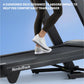 Person wearing white sneakers and black leggings running on NordicTrack treadmill with cushioned black deck against blue back