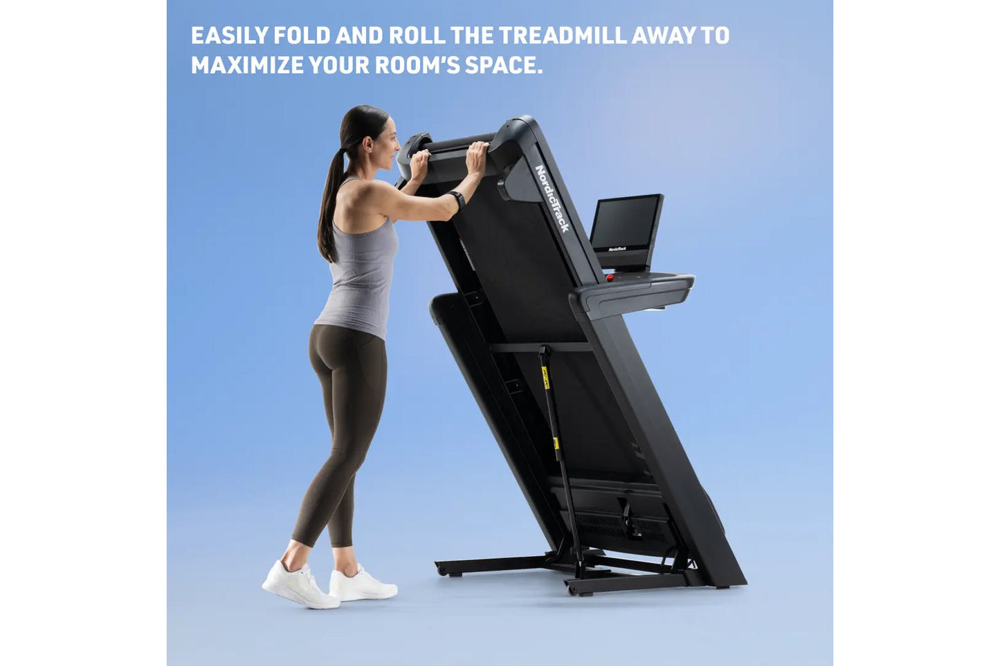 Woman folding black NordicTrack treadmill with digital display, demonstrating compact storage capability