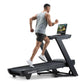 Man running on black NordicTrack treadmill with tablet display, wearing gray sleeveless shirt and black shorts