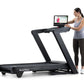 Woman wearing gray tank top and black leggings using black NordicTrack treadmill with attached tablet display showing fitness