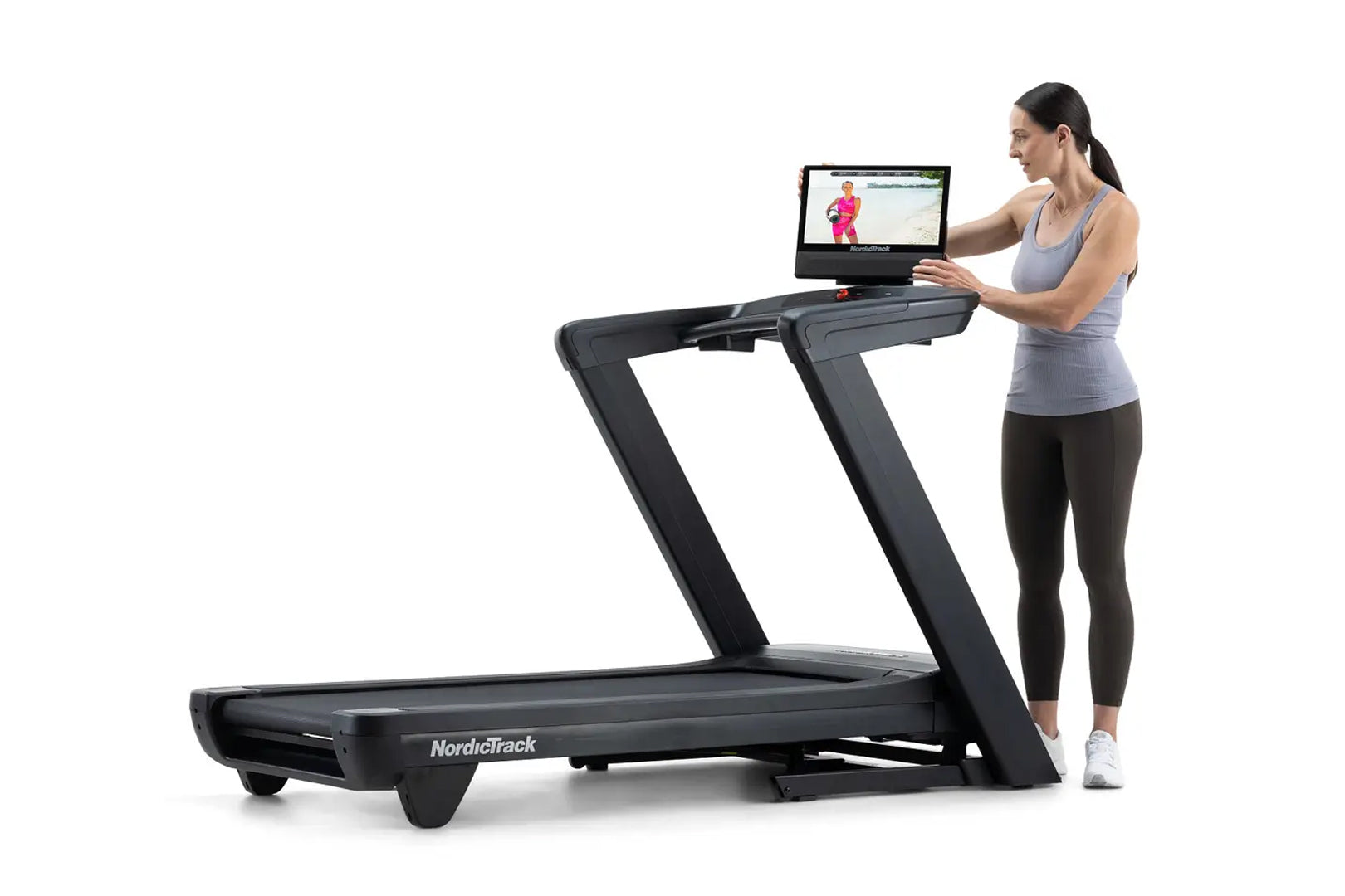 Woman wearing gray tank top and black leggings using black NordicTrack treadmill with attached tablet display showing fitness
