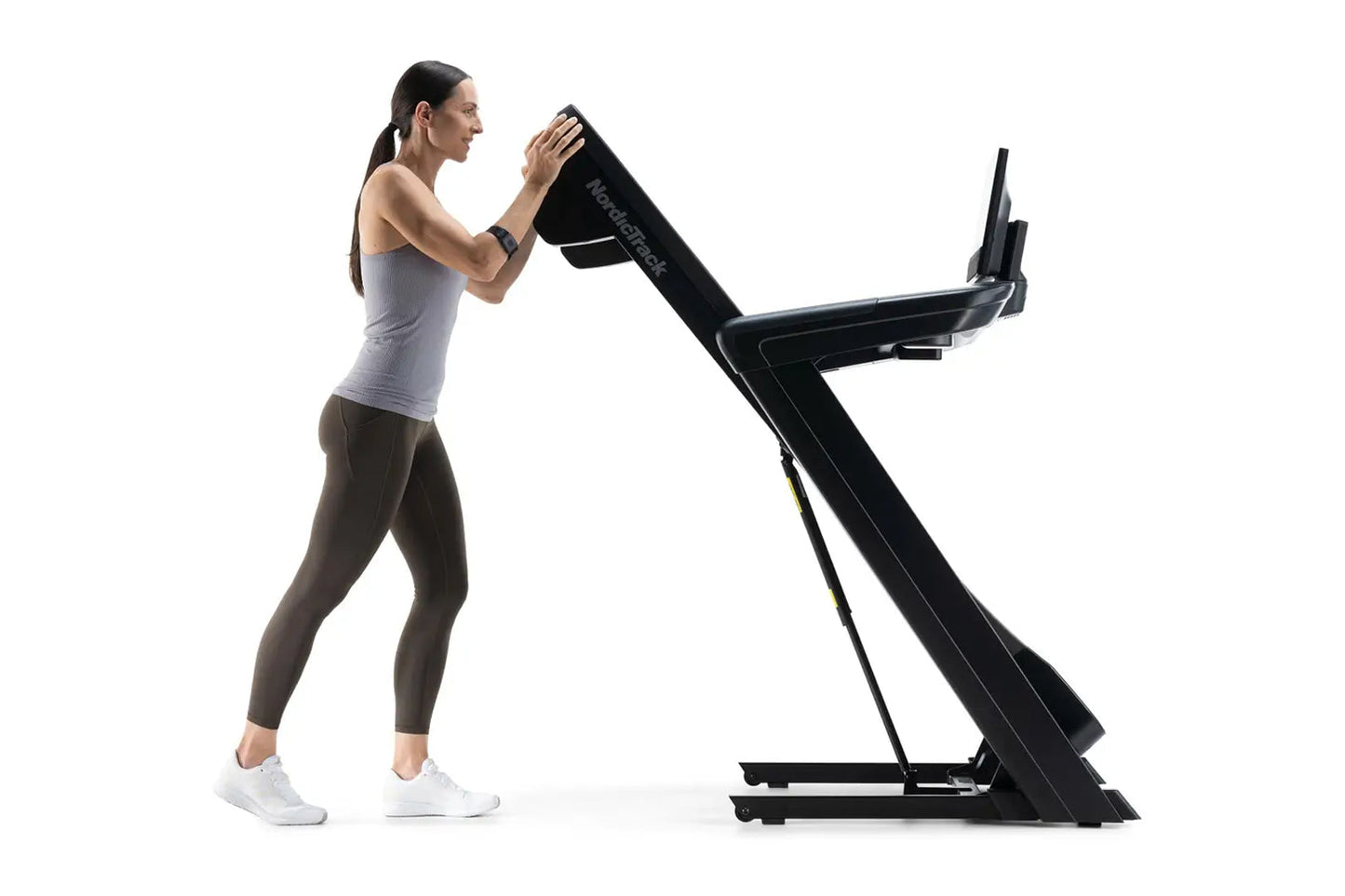 Woman using black NordicTrack treadmill, wearing gray tank top and brown leggings, demonstrated on white background