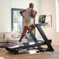 Man running on black NordicTrack treadmill with tablet display in bright home gym with couch and windows