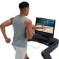 Man wearing gray sleeveless tank top running on black NordicTrack treadmill with display screen showing outdoor workout video