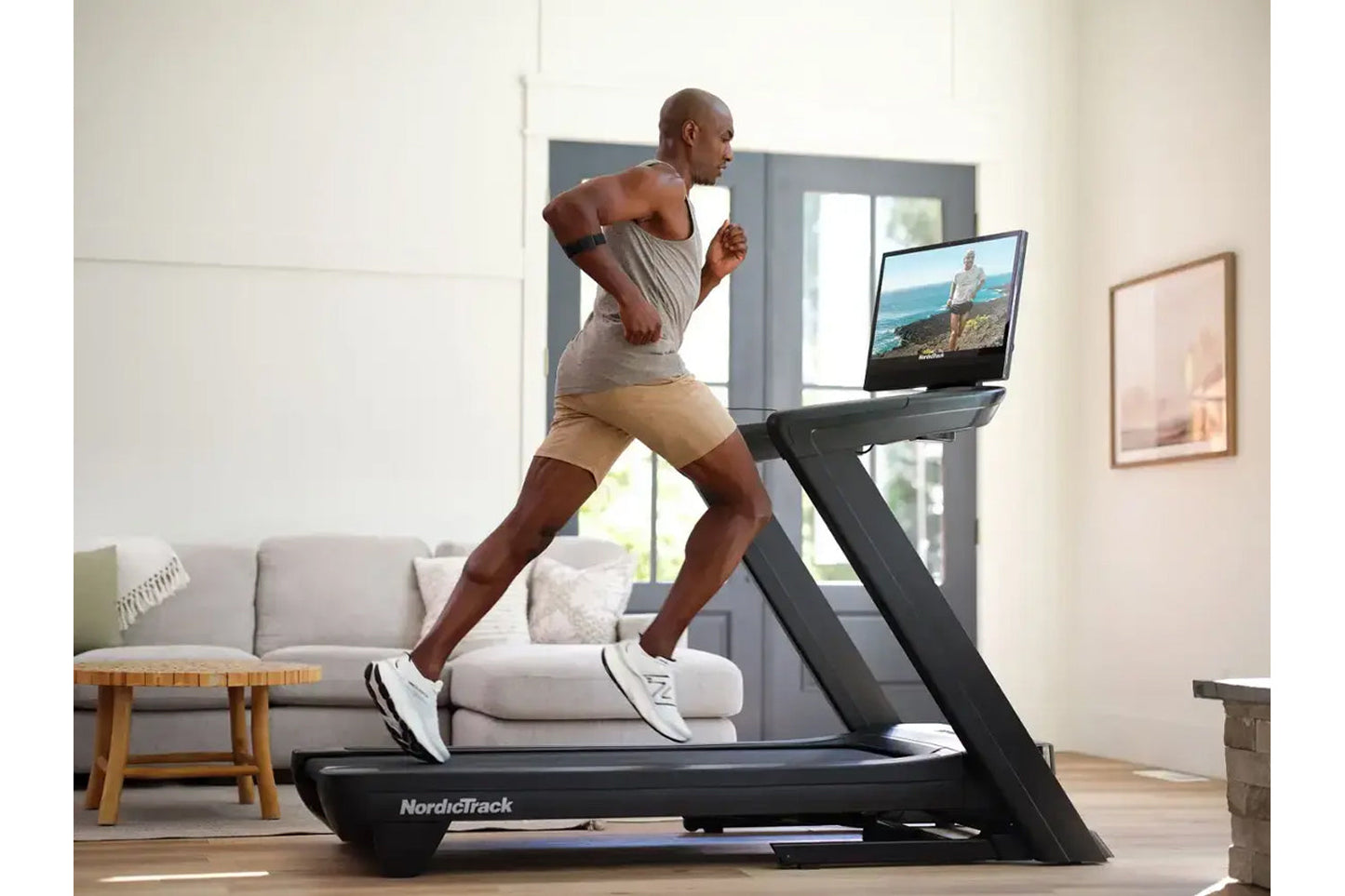 Man running on NordicTrack black treadmill with touchscreen displaying outdoor scenery in modern living room