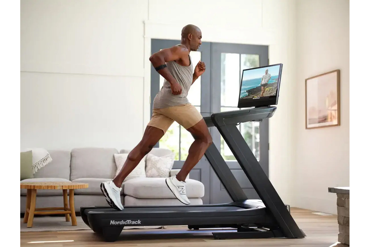 Man running on NordicTrack black treadmill with touchscreen displaying outdoor scenery in modern living room