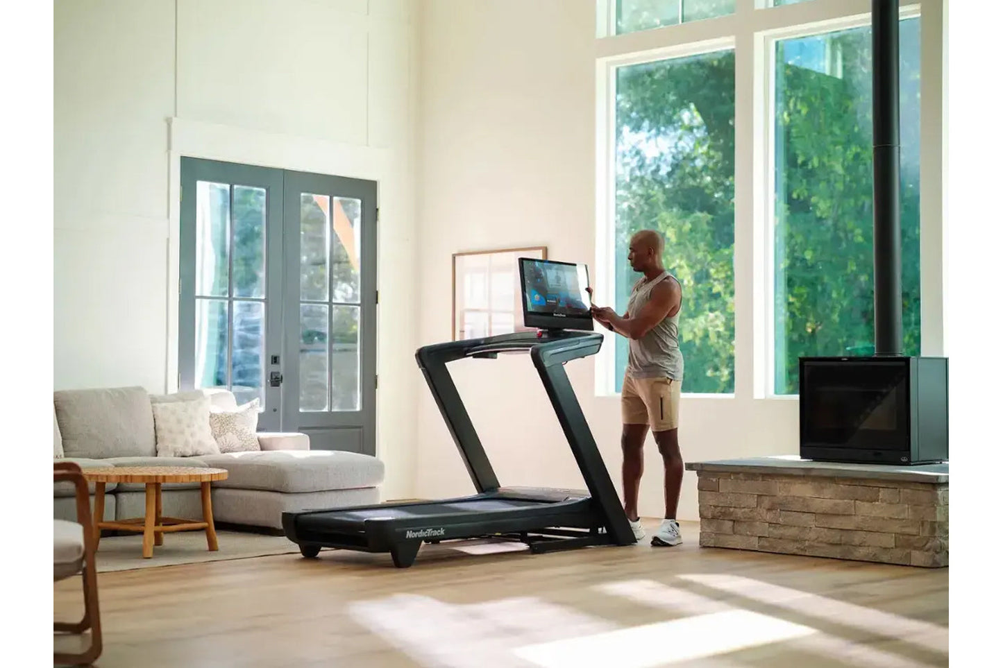 Man using black NordicTrack treadmill with digital display in modern living room with large windows