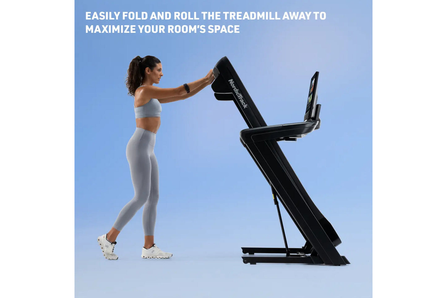 Woman in white sports bra and leggings using folded black NordicTrack treadmill on blue background
