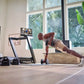 Man performing plank exercise on floor in modern home gym with NordicTrack treadmill, dumbbells, and potted plant visible