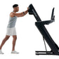 Man wearing gray tank top and white shorts using black NordicTrack treadmill with incline, demonstrating workout form