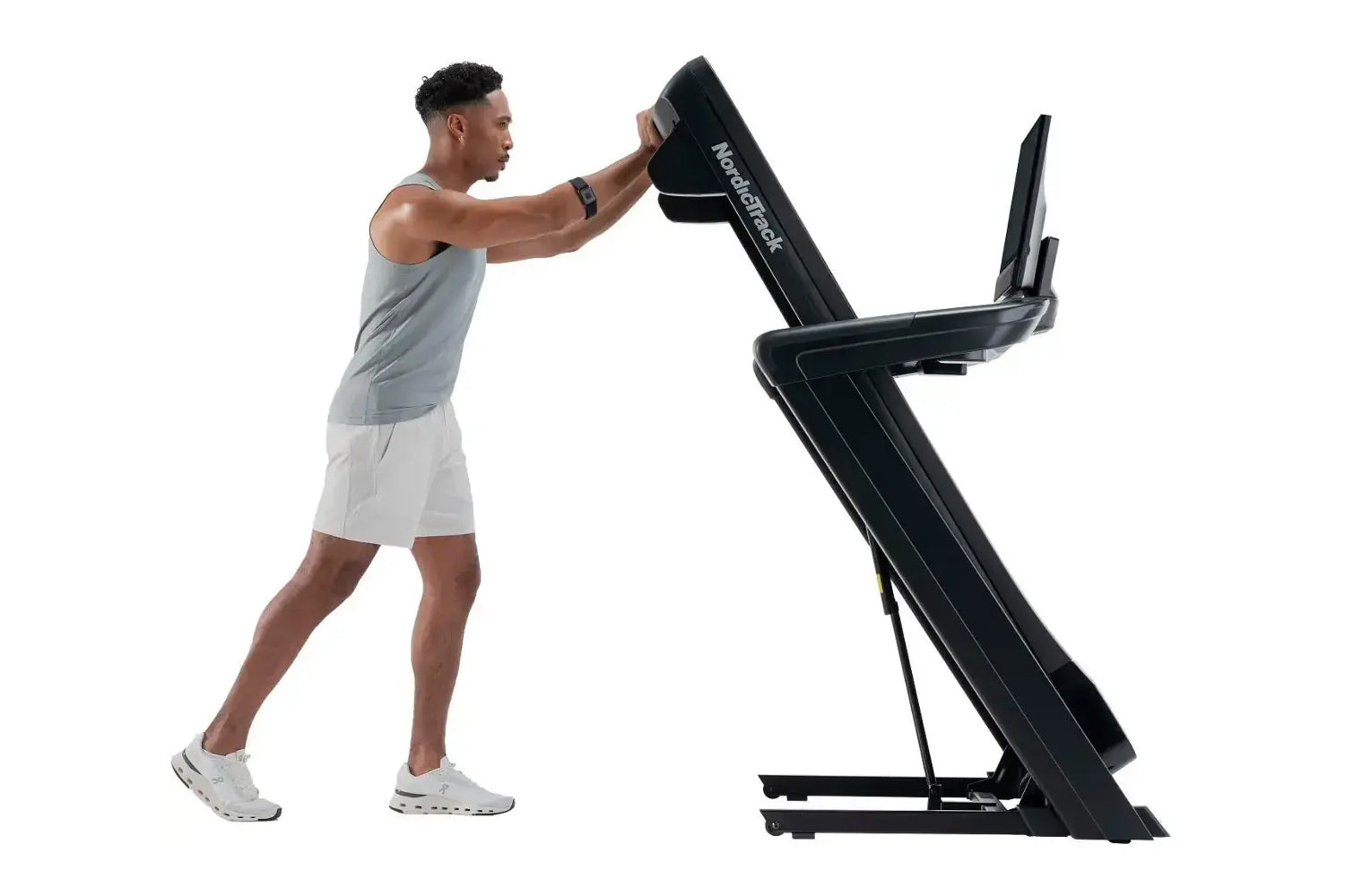 Man wearing gray tank top and white shorts using black NordicTrack treadmill with incline, demonstrating workout form