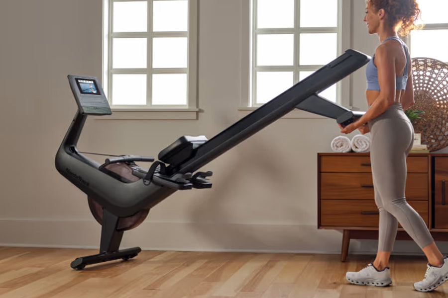 Woman in blue sports bra and beige leggings using black NordicTrack RW600 rowing machine with digital display in bright home 