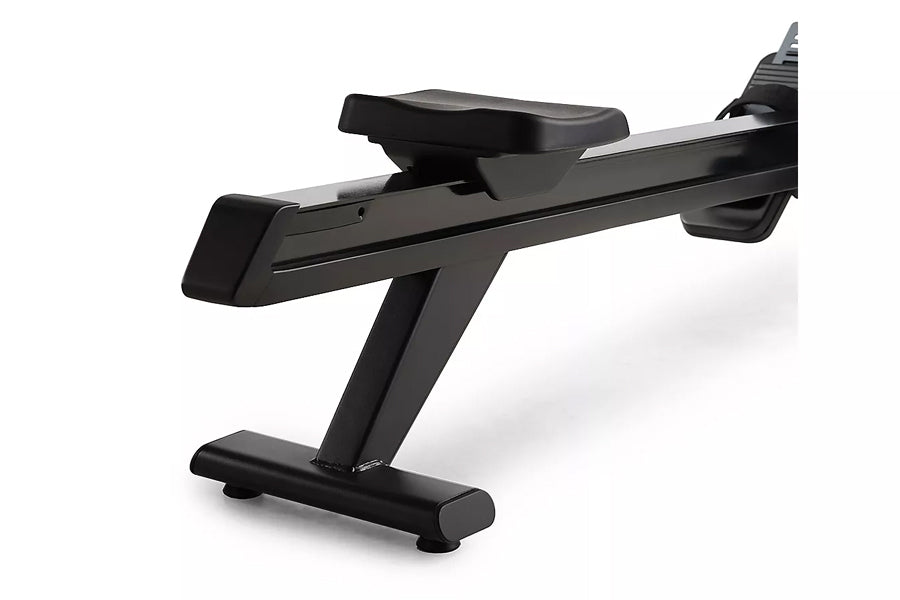 Black stationary rowing machine with padded seat, foot pedals, and horizontal resistance rail on white background