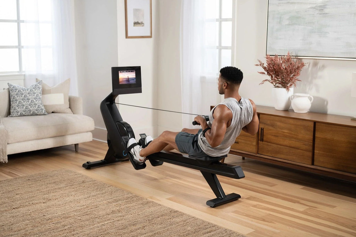 Black NordicTrack RW700 rowing machine with digital display, used by man in home living room