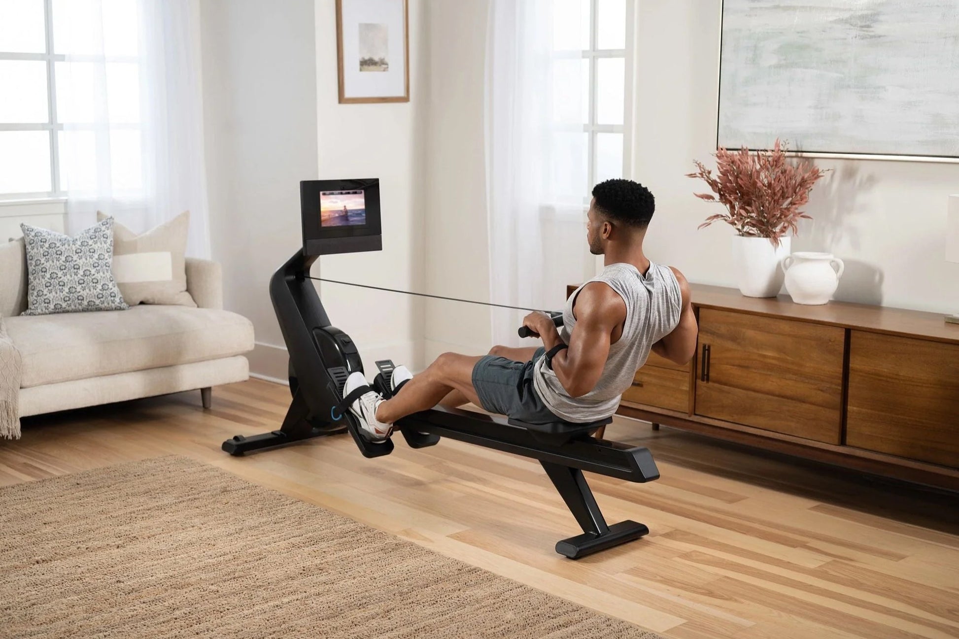 Black NordicTrack RW700 rowing machine with digital display, used by man in home living room