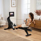 Woman using black NordicTrack rowing machine with digital display in modern home living room