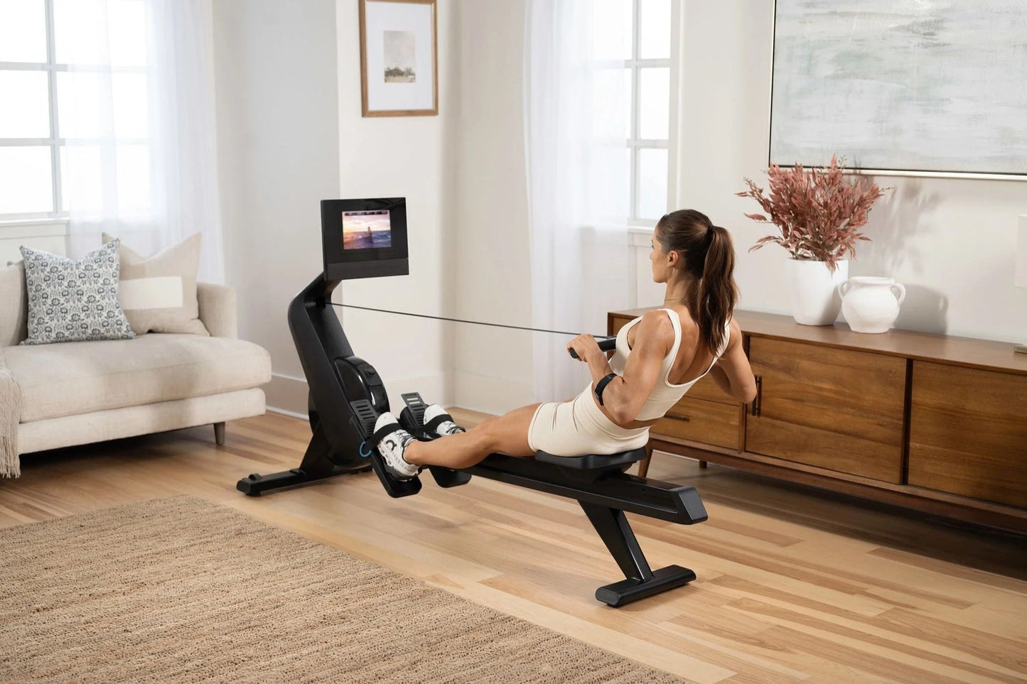 Woman using black NordicTrack rowing machine with digital display in modern home living room