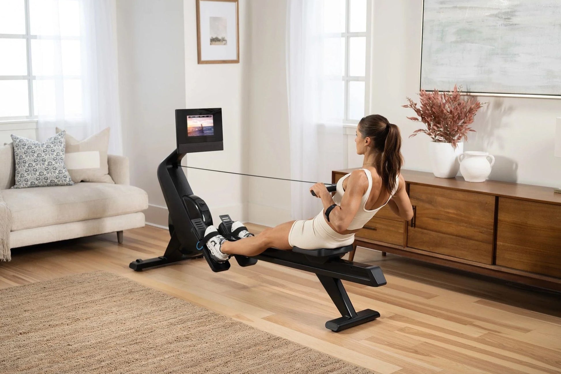 Woman using black NordicTrack rowing machine with digital display in modern home living room