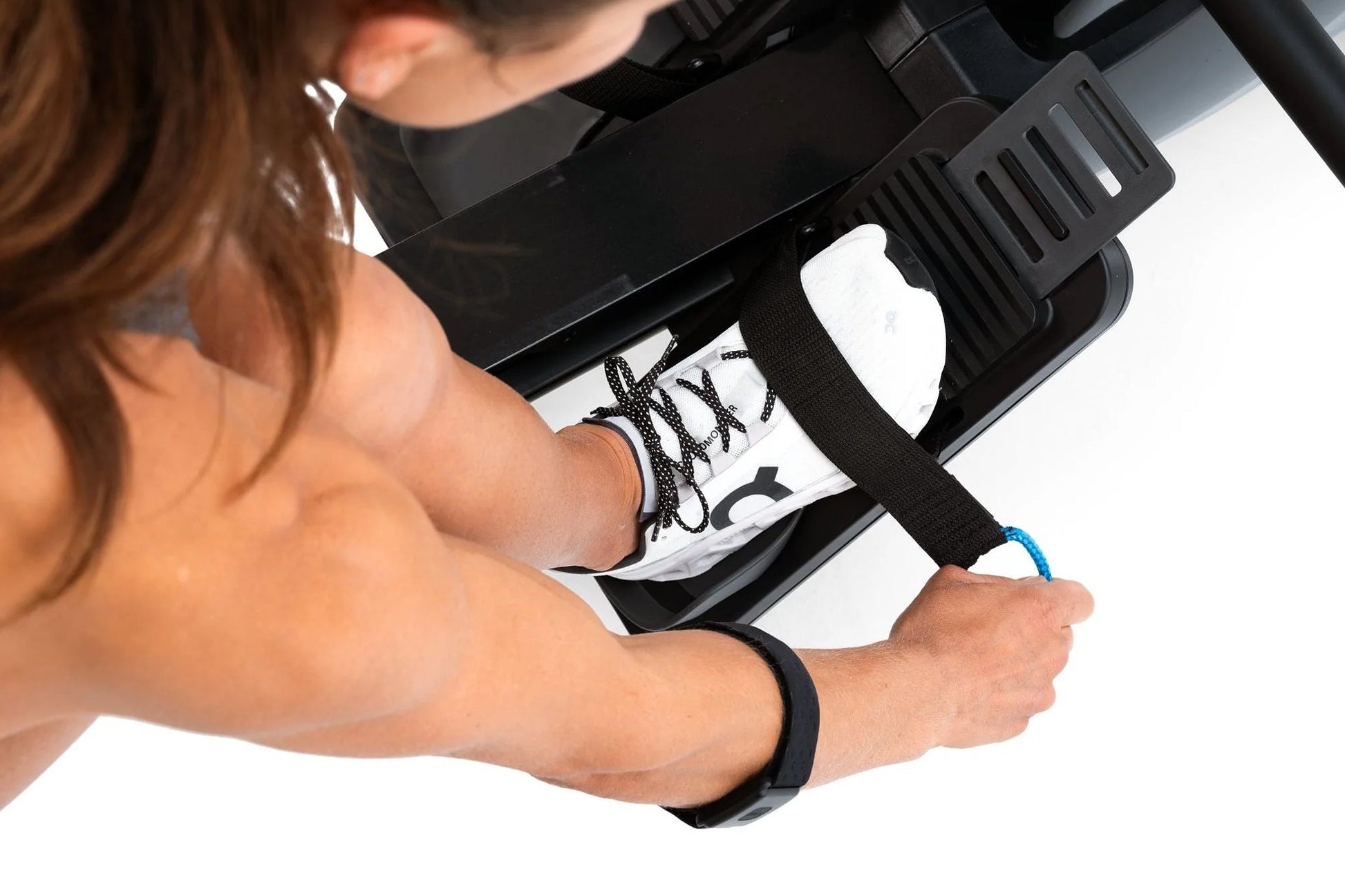 Person's hands gripping black rower footrest with white and black athletic shoe on pedal