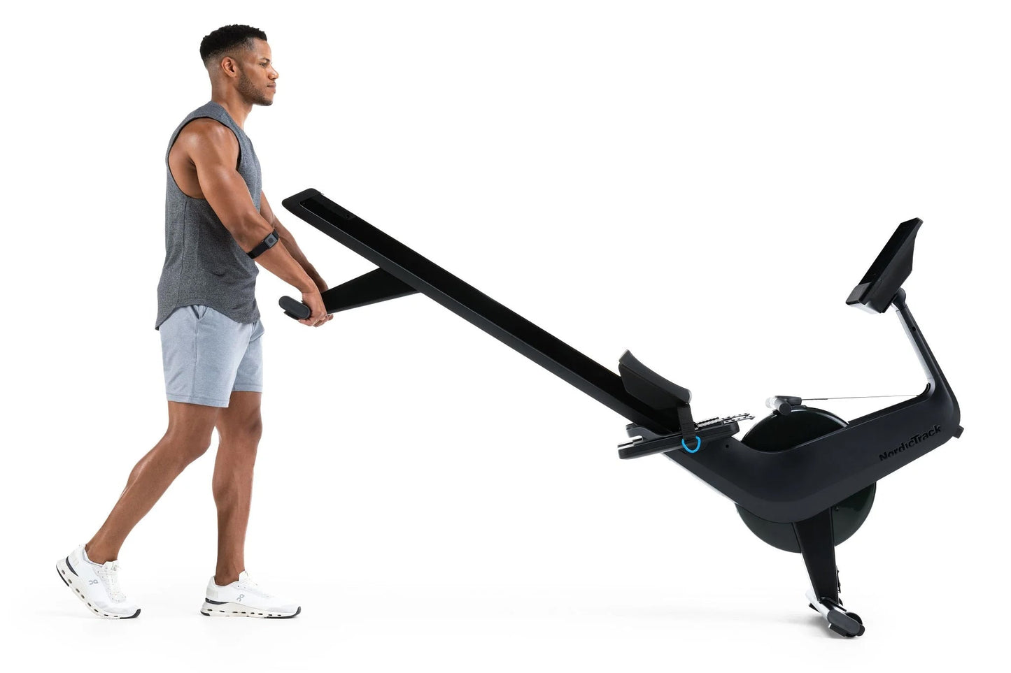 Man using black NordicTrack RW700 rowing machine, wearing gray tank top and light blue shorts