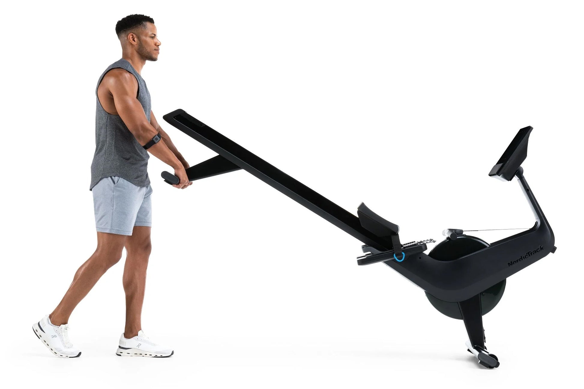 Man using black NordicTrack RW700 rowing machine, wearing gray tank top and light blue shorts