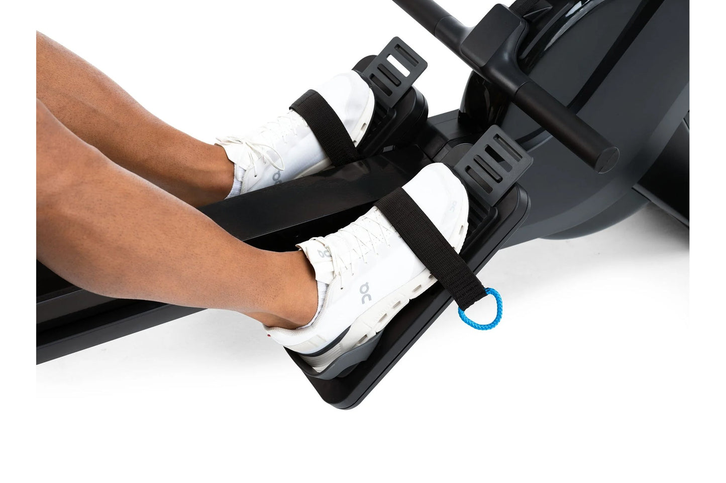 Person wearing white sneakers on black rowing machine foot pedals with adjustable straps