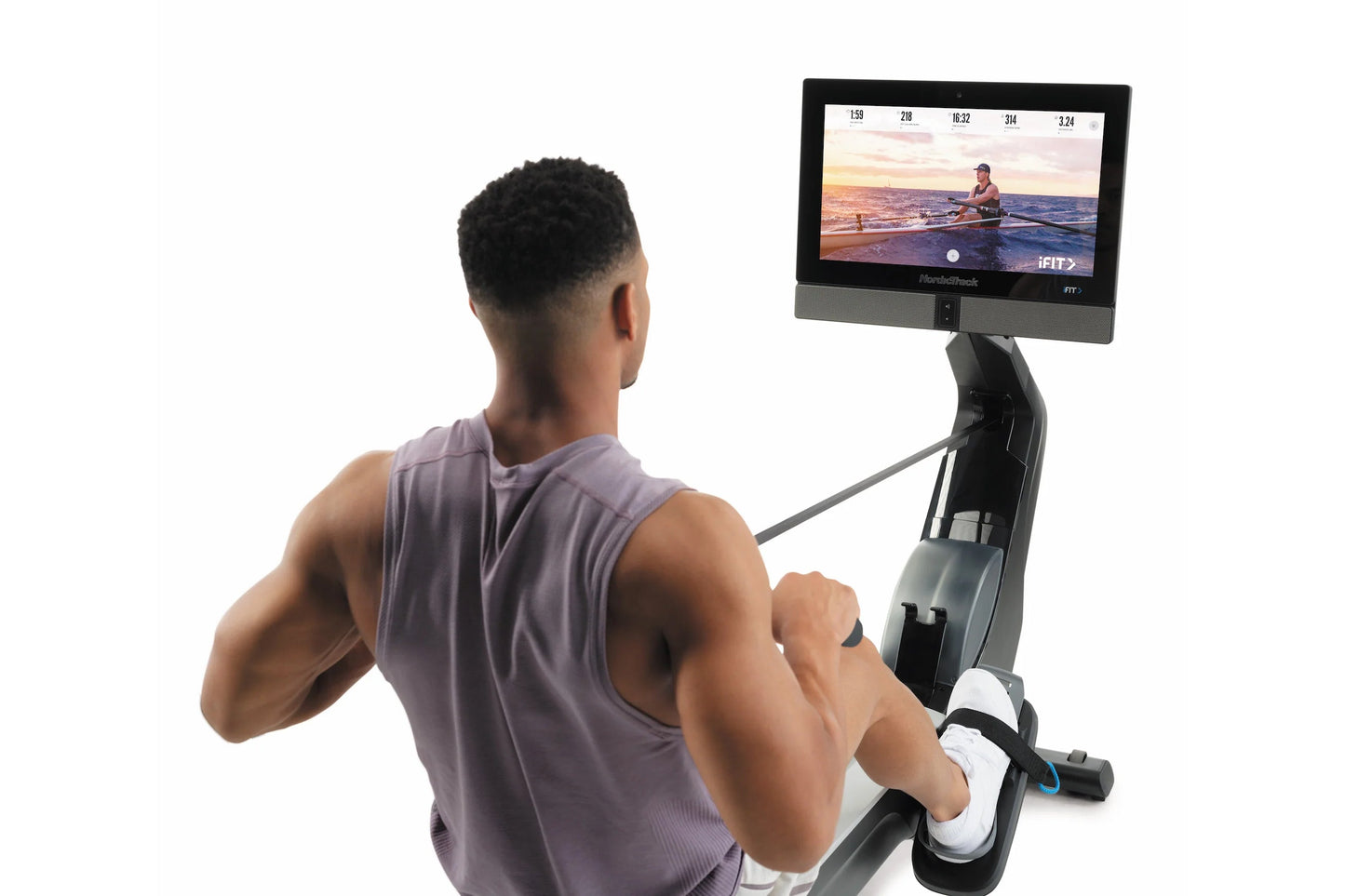 Man using black and gray NordicTrack rowing machine with touchscreen display showing fitness class, worn against white backgr