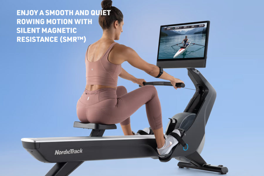 Woman in pink sports bra and leggings using black NordicTrack rowing machine with tablet displaying water rowing scene agains