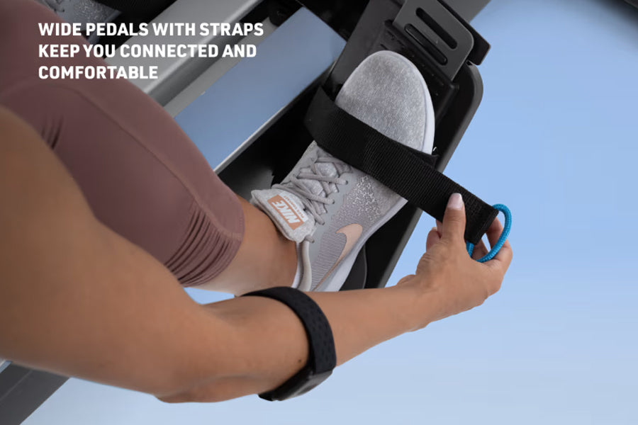 Foot pedal with black adjustable strap attached to NordicTrack rowing machine, worn by model's foot