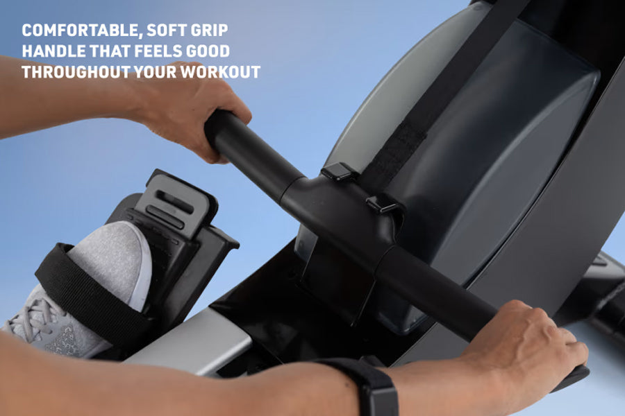 Hands gripping black soft-grip handle of rowing machine, worn by person in light gray shoe, against blue sky background