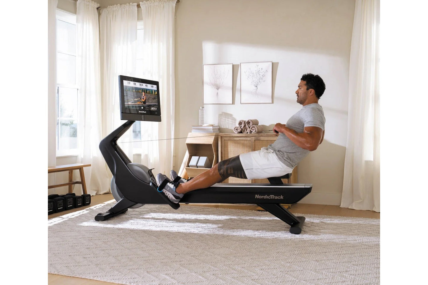Man using black NordicTrack rowing machine with digital screen in home gym setting