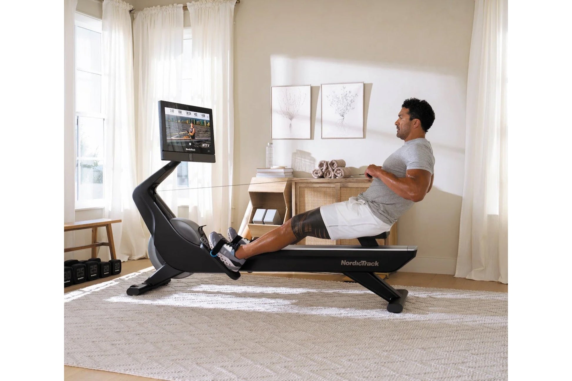Man using black NordicTrack rowing machine with digital screen in home gym setting