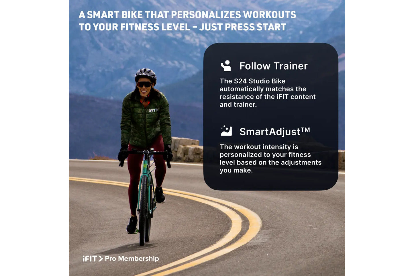 Cyclist riding teal and black studio bike outdoors on mountain road, wearing green jacket and burgundy leggings with helmet a
