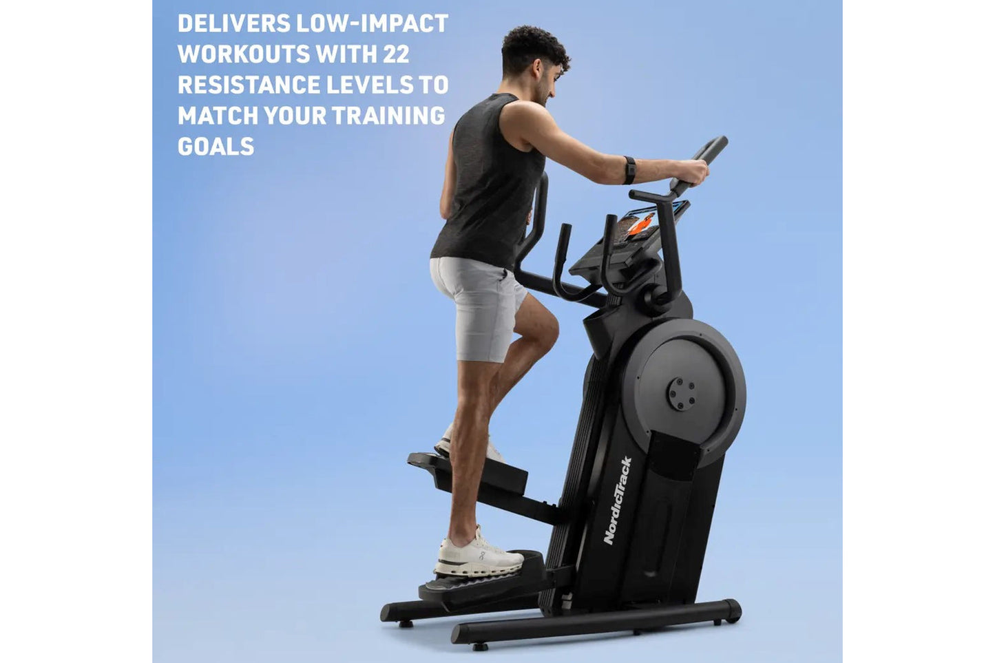 Man using black NordicTrack step climber with digital display, wearing charcoal tank top and white shorts, on blue background