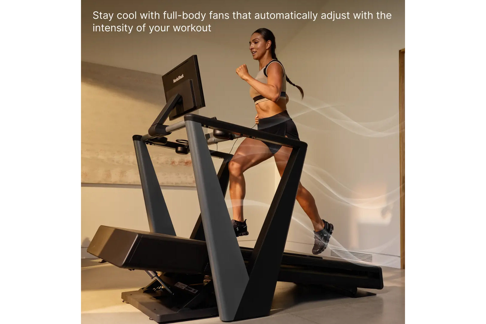 Woman running on black NordicTrack treadmill with monitor, wearing black sports bra and shorts