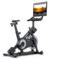 NordicTrack X24 black indoor exercise bike with attached tablet displaying sunset cycling video on white background