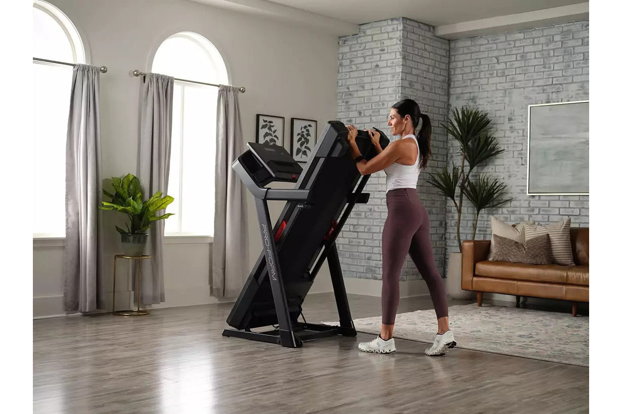 Black ProForm Carbon TLS treadmill with red accents, woman in white tank top and burgundy leggings running on treadmill in mo