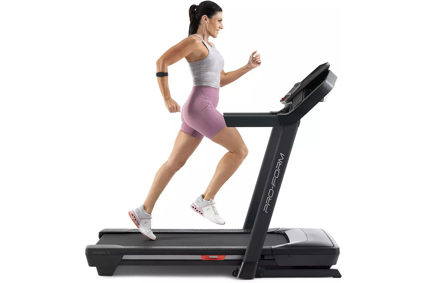 Woman running on black ProForm Carbon TLS treadmill wearing gray tank top, mauve shorts, and white sneakers with fitness trac