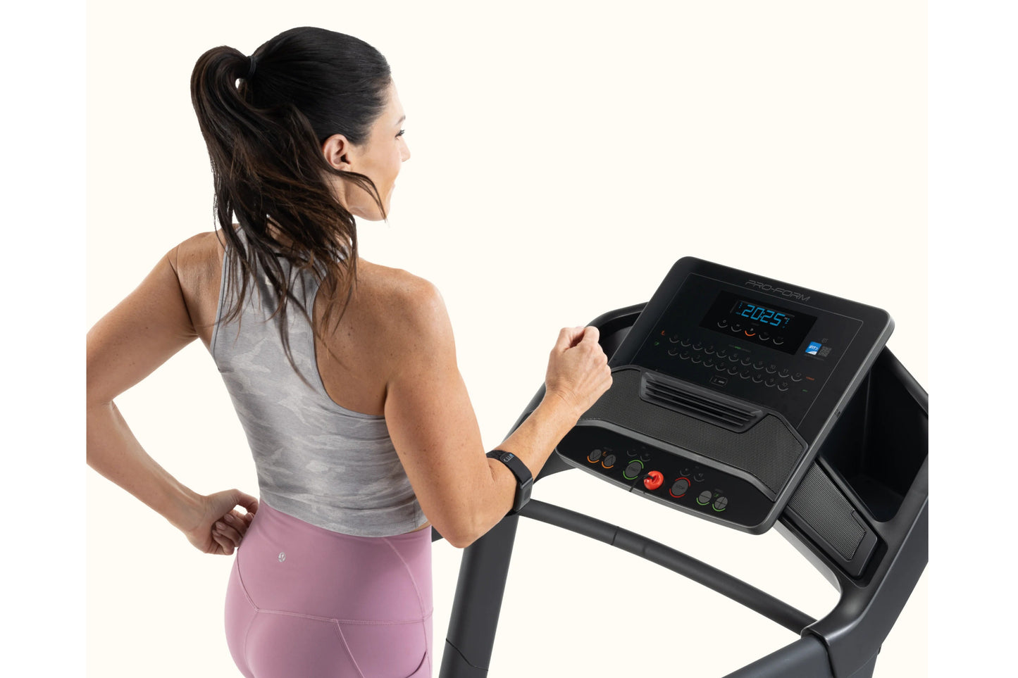 Woman in gray tank top and pink leggings running on black ProForm treadmill with digital display, shown from side profile