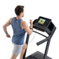 Man running on black ProForm treadmill with digital display, wearing blue sleeveless shirt and gray shorts